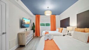 Una habitación de hotel con cama, televisión, cómoda de madera y ventana con cortinas.