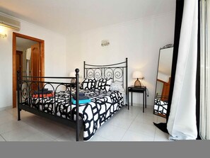 A bedroom with a four-poster bed, a bedside table with a lamp, a mirror, and a door leading to another room. - Roger de Flor in Puerto Pollensa (Pollença)