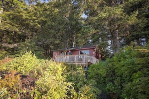 A cabin surrounded by dense forest, with a balcony and a chimney.