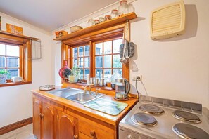 Une cuisine avec des meubles de rangement en bois, un  évier, une cuisinière et une fenêtre avec des stores.