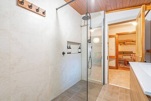 A bathroom with a glass shower enclosure, a wooden shelf with decorative items, and a visible towel rack. - Bobs Cottage Nostalgic Charm and Homely Comfort (Dynnyrne)