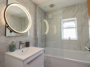 Un baño con un lavabo blanco, un espejo con luz, una ducha y una ventana.