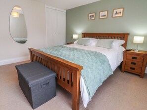 Un dormitorio con cama de madera, una mesita de noche con lámpara, un pequeño banco y un espejo en la pared.