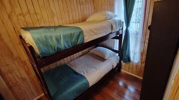 A bunk bed with a green blanket and white bedding in a room with wooden walls and a wooden floor.