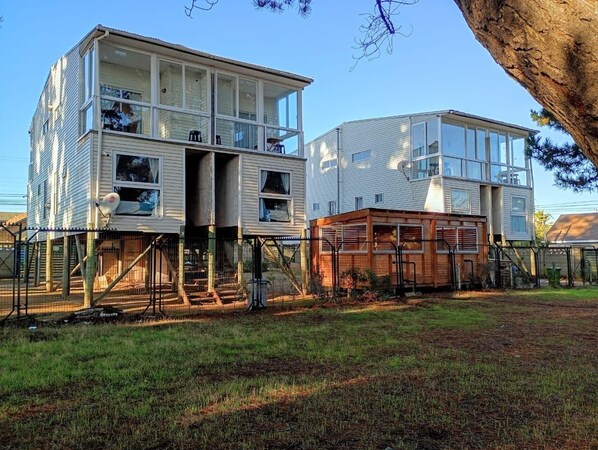 Two multi-story buildings with balconies, a fenced yard, and a tree.