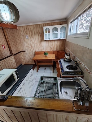 A compact kitchen with a wooden table, a microwave, a kettle, a sink, and a window.