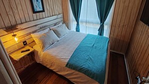 Habitació amb panells de fusta, un llit, una taula de nit, un comandament a distància i televisió penjada a la paret.