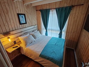 A wooden-paneled room with a bed, a nightstand, a remote control, and a wall-mounted TV.