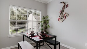 Un coin repas avec une table et des bancs, une fenêtre avec des stores, une plante et un saxophone décoratif accroché au mur.