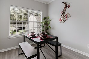 A dining area with a table and benches, a window with blinds, a plant, and a saxophone decoration on the wall. - SAVE BIG/ Walkable Uptown Dallas 2BR/ Nightlife (Dallas)