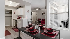 Une cuisine moderne avec des meubles blancs, un coin repas doté d’une table noire et de sets de table rouges, et un canapé rouge en arrière-plan.