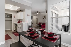 A modern kitchen with white cabinets, a dining area with a black table and red placemats, and a red sofa in the background. - SAVE BIG? Walkable Uptown Dallas 2BR/ Nightlife (Dallas)