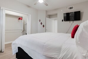 A bedroom with a bed, a ceiling fan, a TV mounted on the wall, and a door with a coat rack. - SAVE BIG/ Walkable Uptown Dallas 2BR/ Nightlife (Dallas)