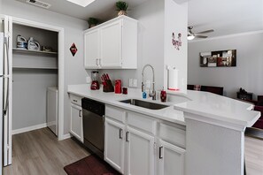 Una cocina moderna con armarios blancos, lavavajillas, fregadero y encimera con diversos utensilios de cocina.