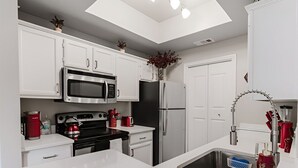 Une cuisine moderne avec des meubles blancs, des appareils en acier inoxydable, un puits de lumière et un îlot central.