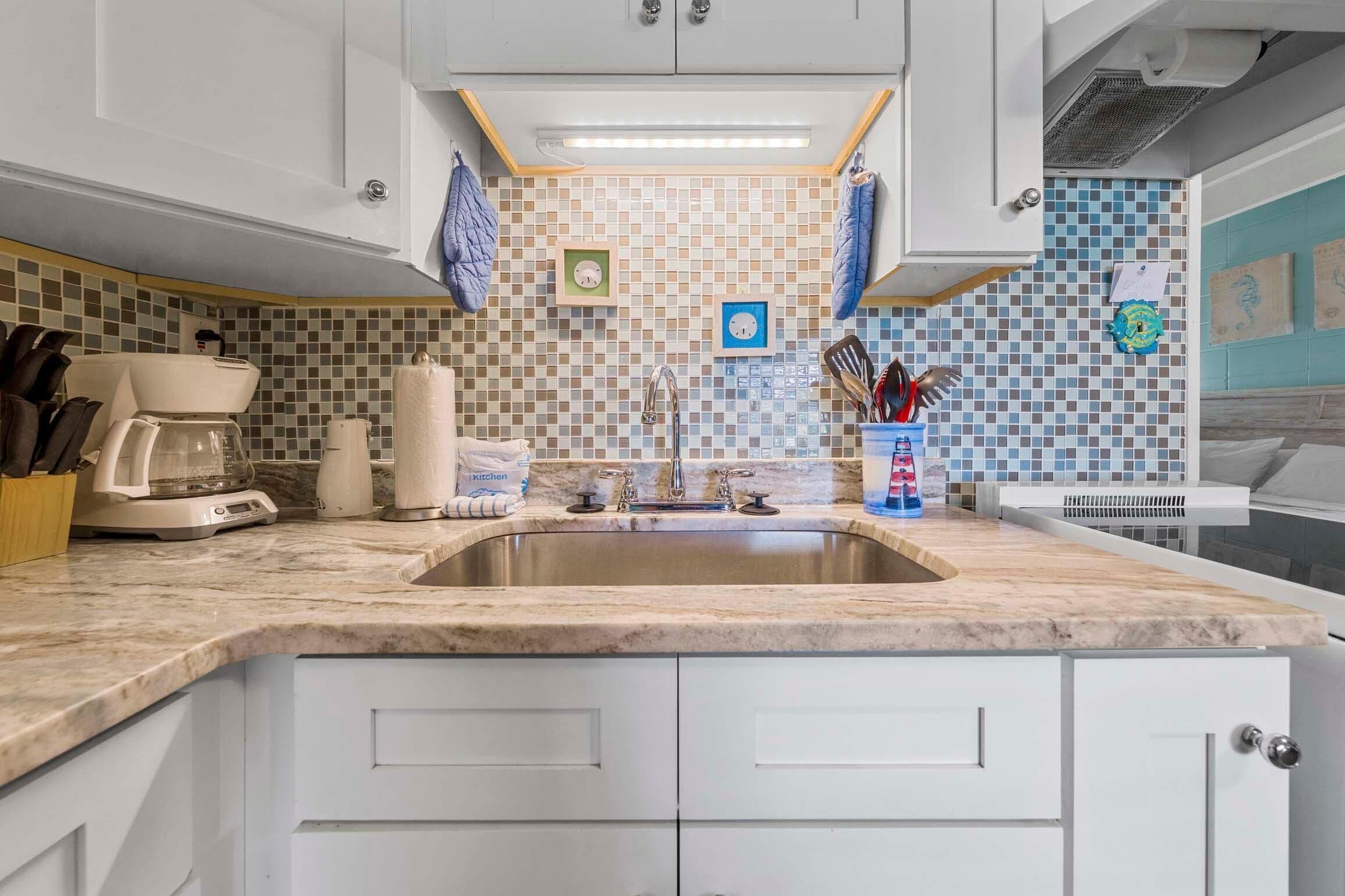 A kitchen with a marble countertop, white cabinets, a stainless steel sink, and a tiled backsplash.