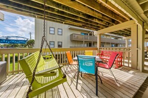 A wooden deck with a swing, a table with chairs, and a view of a building with balconies. - Gulf Village 101 (Gulf Shores)
