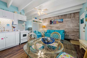 A kitchen with white cabinets, a stove, and a dining area with a glass table and chairs. - Gulf Village 101 (Gulf Shores)
