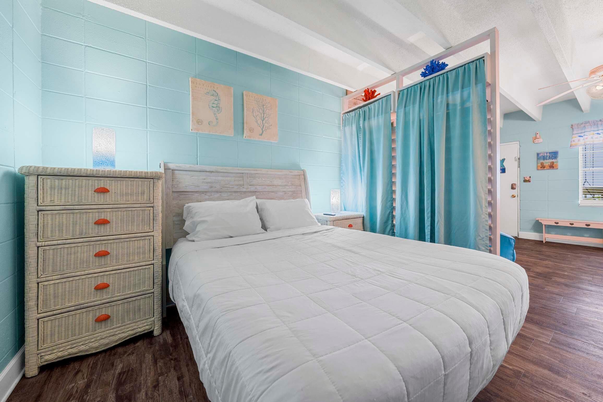 A bedroom with a bed, a dresser, a nightstand, and a window with curtains.