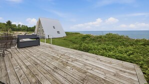 A wooden deck with a table and chairs, overlooking a body of water and a grassy area. - Juniper Presents: Chalet #8 3BR Lakefront with Resort Amenities (Stevensville)