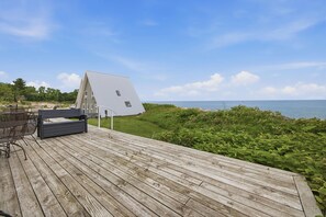 Une terrasse en bois avec une table et des chaises, donnant sur une étendue d’eau et une zone herbeuse.