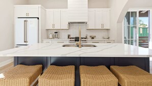 Une cuisine moderne avec des meubles blancs, un îlot central doté de tabourets et une grande fenêtre.