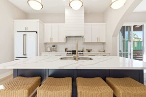 A modern kitchen with white cabinetry, a central island with stools, and a large window. - Juniper Presents: NEW!Elevated Lake Living, Walk to Beach, EV & Pool (Union Pier)