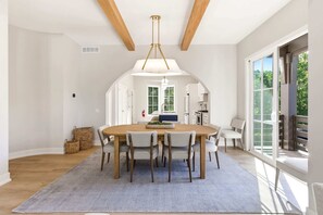 A dining area with a wooden table, six chairs, a hanging light fixture, and a view of the outdoors through large windows. - Juniper Presents: NEW!Elevated Lake Living, Walk to Beach, EV & Pool (Union Pier)
