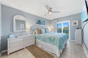 A bedroom with a bed, a dresser, a ceiling fan, a TV, and a window with a view. - Grand Caribbean 117 (Orange Beach)