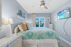 A bedroom with a bed, a ceiling fan, a TV, and a window with a view. - Grand Caribbean 117 (Orange Beach)