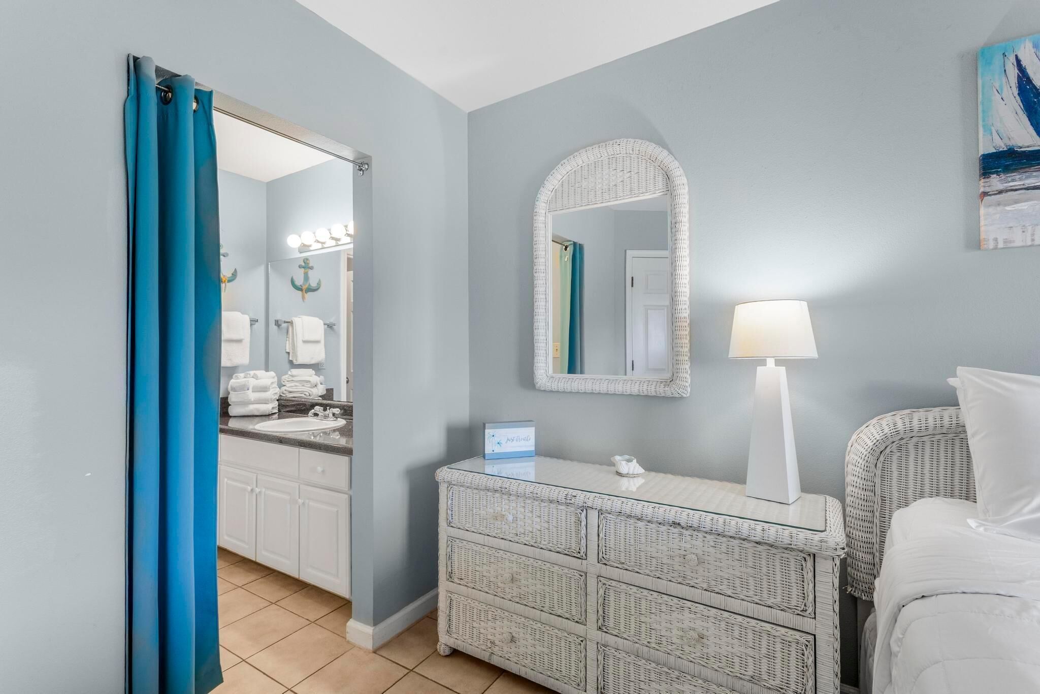 A hotel room with a bathroom, a bed, a dresser, and a lamp.