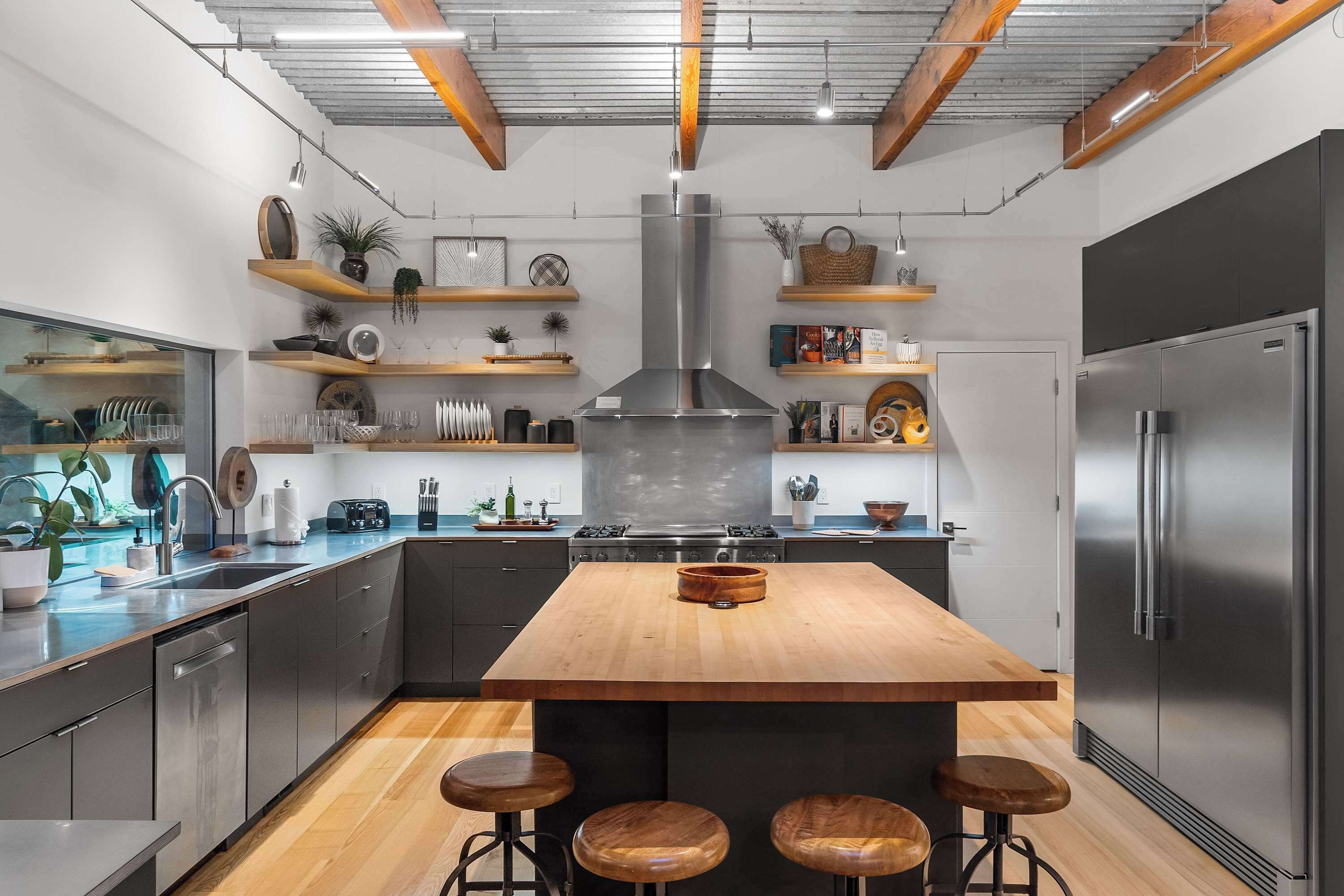 A modern kitchen with a central island, bar stools, stainless steel appliances, and wooden shelves.