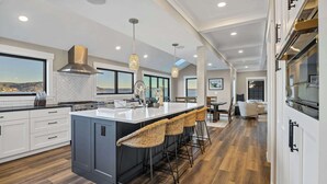 A modern kitchen with a large island, bar stools, and a view of the outdoors. - Waterfront Retreat - Hot Tub, Fireplace, Pier (hoodsport)