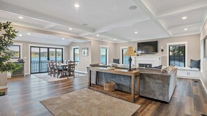A spacious living room with a fireplace, a dining area, and large windows offering a view of the outdoors. - Waterfront Retreat - Hot Tub, Fireplace, Pier (hoodsport)