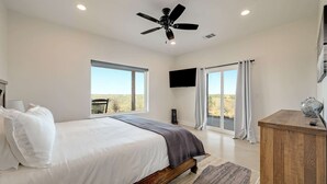 Quarto com cama, ventoinha no teto, televisão e vista para o exterior.