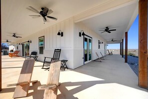 A covered patio area with ceiling fans, outdoor seating, and a view of the desert. - Secluded Hill Country Getaway • Stunning Views + Fire Pit • 15 Min to Main St (Fredericksburg)