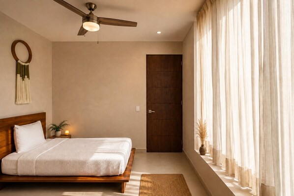 A bedroom with a bed, a ceiling fan, a door, and a window with curtains.