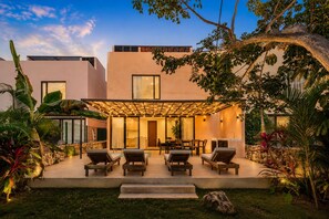 A modern house with a patio, outdoor seating, and lush greenery.