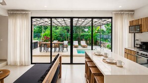 Una cocina moderna con una isla grande, puertas de vidrio correderas a un patio y vistas a una piscina y jardín.
