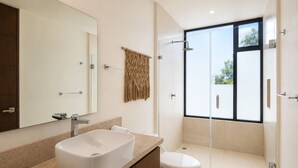 Un baño moderno con un espejo grande, una bañera independiente, un inodoro y una ducha con mampara de vidrio.