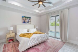 Ein Schlafzimmer mit Bett, Nachttisch, Gemälde, Deckenventilator und Blick ins Freie.