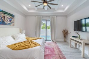 Ein Schlafzimmer mit einem Bett, Deckenventilator, Fernseher, Schreibtisch und Blick ins Freie.