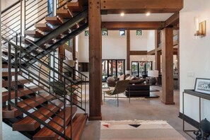 Een modern interieur met een houten trap, een zithoek met een bank en stoelen, en een uitzicht door grote ramen.