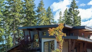 Un bâtiment moderne à deux étages, doté de grandes fenêtres, d’une façade en bois et d’un jardin paysager à l’avant, avec de hautes herbes et un arbre.