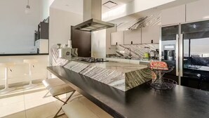Une cuisine moderne dotée d’un plan de travail en marbre, d’appareils électroménagers en acier inoxydable et d’un grand îlot central avec des tabourets de bar.