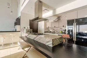 A modern kitchen with a marble countertop, stainless steel appliances, and a large island with bar stools. - Beautiful beachfront penthouse with private pool (Puerto Vallarta)