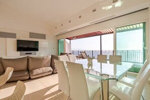 Uma sala de estar moderna com sofá, poltronas, mesa de vidro, televisão e varanda com vista.