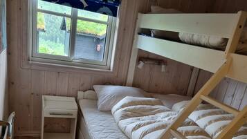 A bunk bed room with a window, a small bedside table, and a wooden floor.
