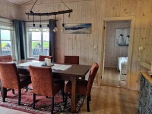 Un'area pranzo con un tavolo di legno, sedie rosse, un tappeto decorato e vista su una casa dalla finestra.