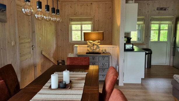 A wooden interior with a dining table, chairs, a lamp, and a kitchen area. - Myrkdalen stay (Myrkdalen)